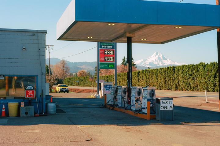 A gas station with a snow-capped mountain in the background is visible under a clear sky.