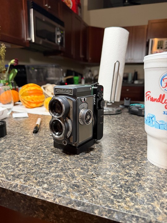 A Rolleiflex camera is on a kitchen counter next to a paper towel roll and a white cup.