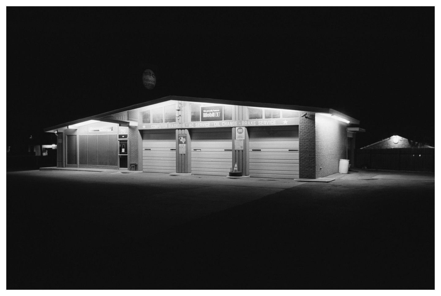 A gas station with three garage doors is illuminated at night.