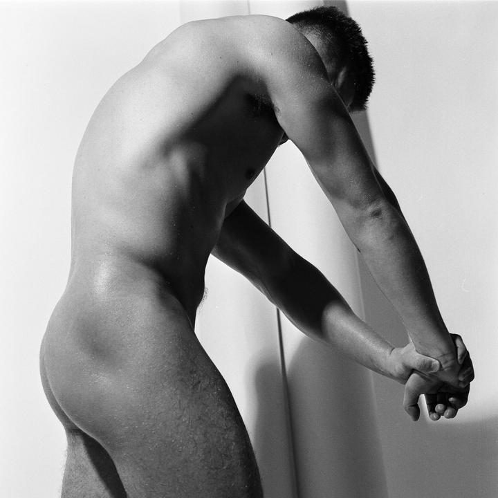 A man with his back arched and hands clasped is shown from the waist up.