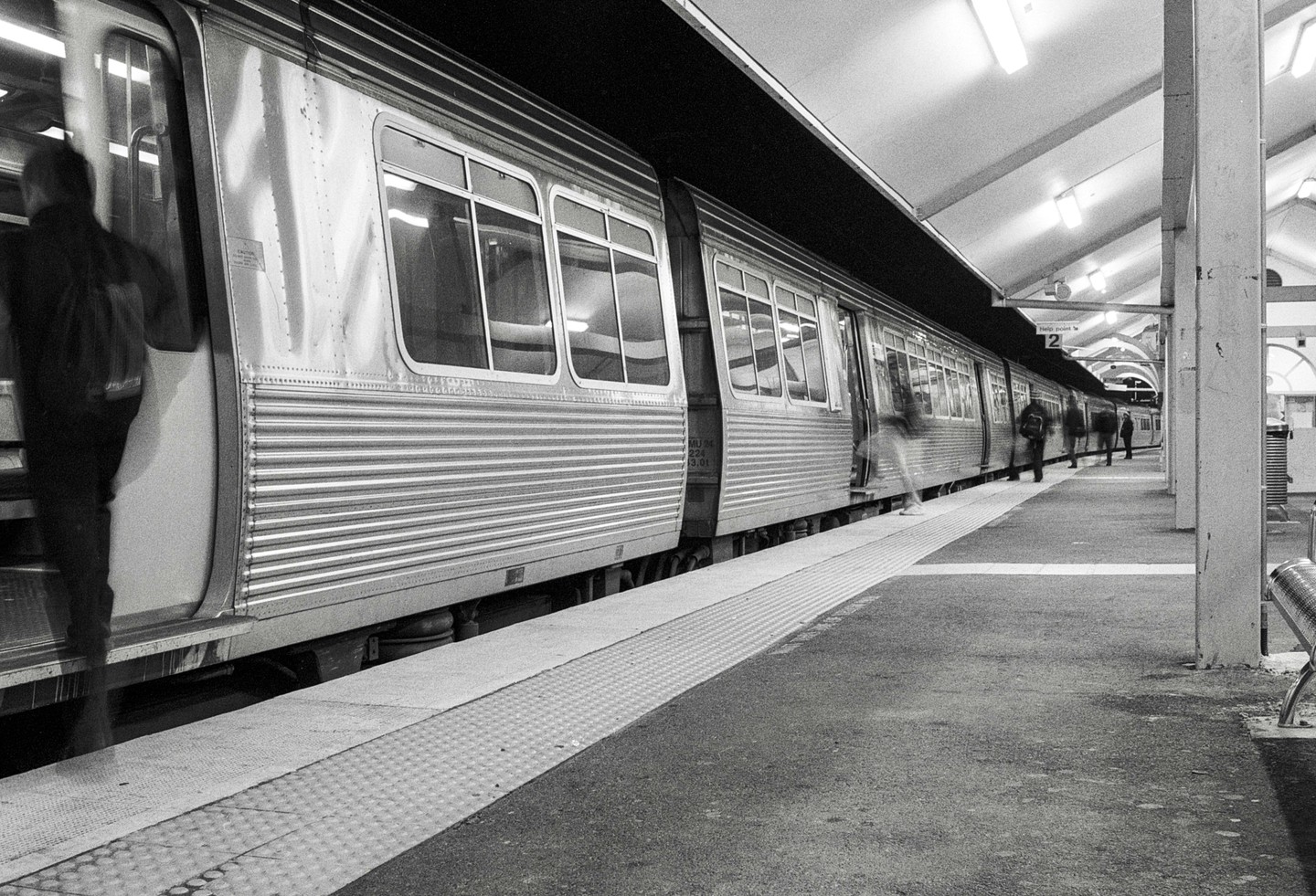 A train is stopped at a station platform with several people boarding and disembarking.