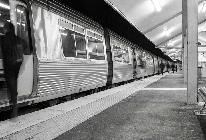 A train is stopped at a station platform with several people boarding and disembarking.