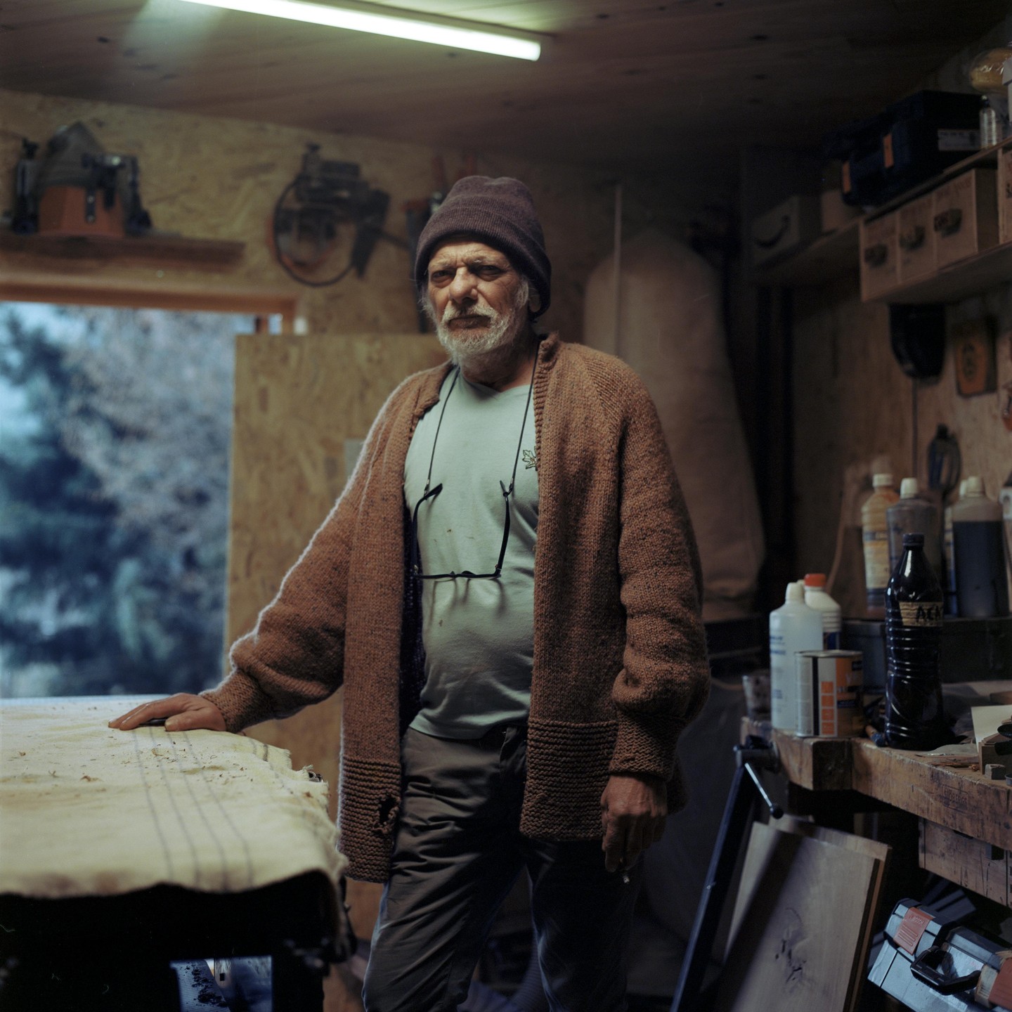 A man with a white beard and a knitted hat stands in a workshop.