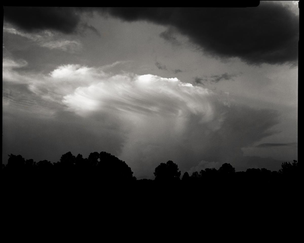 A dramatic sky with swirling clouds looms over a dark silhouette of trees.