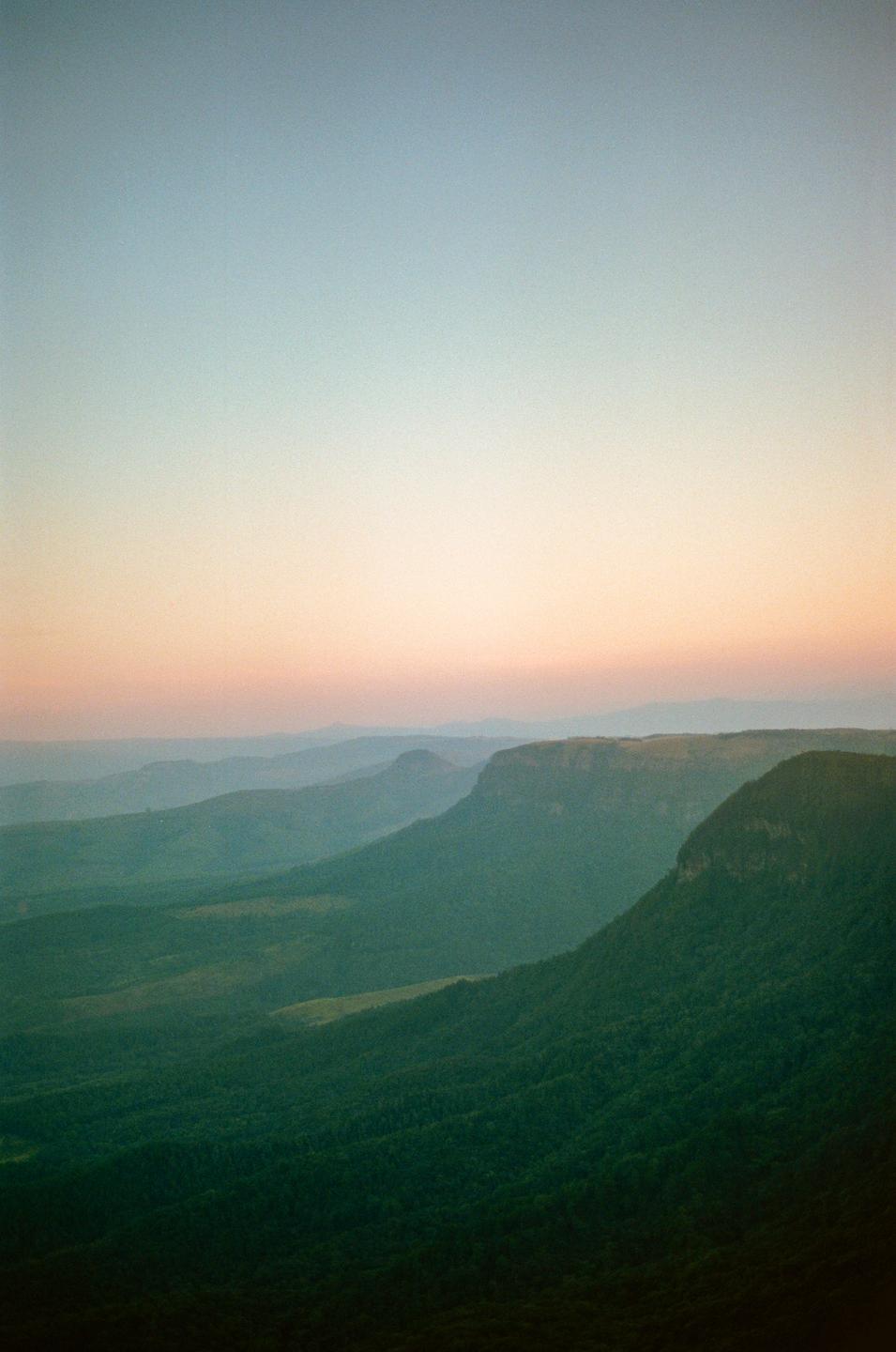 A vast landscape of rolling hills and mountains is visible under a colorful sky at dusk.
