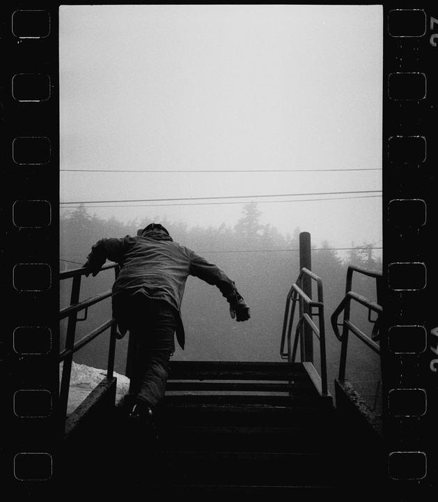 A person climbs a set of outdoor stairs with railings into a hazy, tree-lined background.