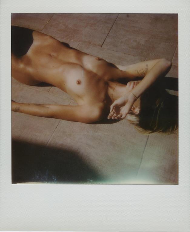 A woman is lying on a tiled surface with her arm covering her face, with shadows cast across her body.