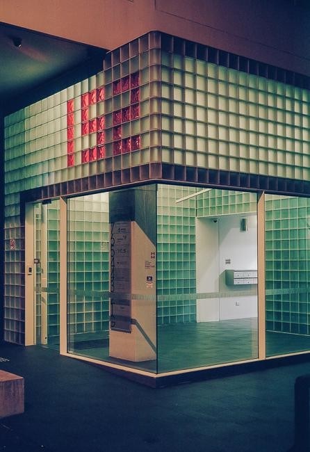 A building with glass block walls and a red pattern on the upper section is visible from a low angle.