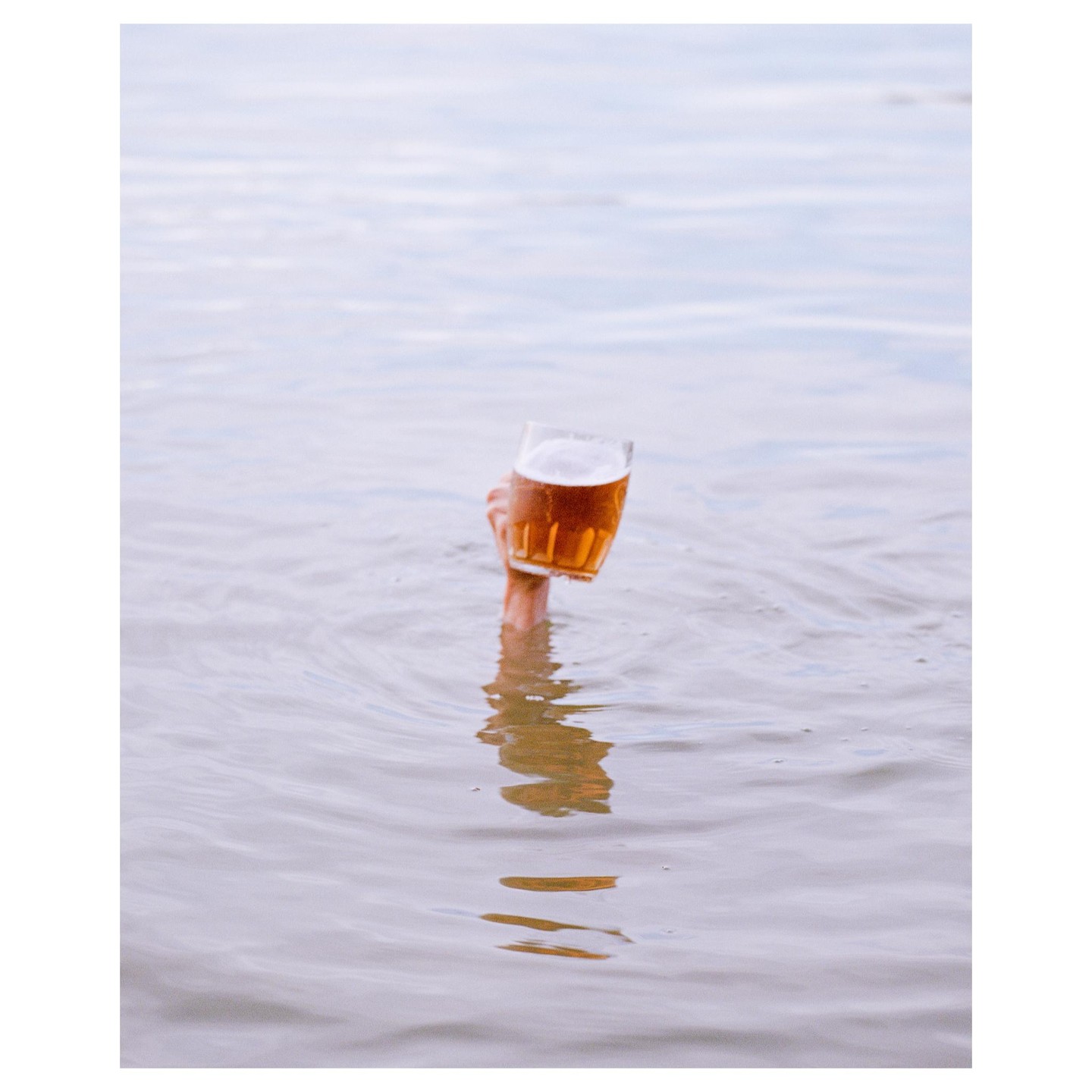 A hand emerges from the water holding a glass of beer.