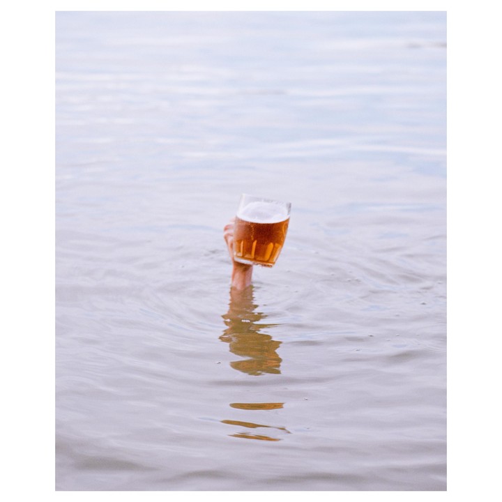 A hand emerges from the water holding a glass of beer.