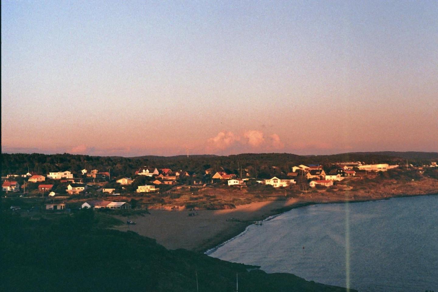 A coastal town with houses and a beach is visible under a colorful sky at dusk.