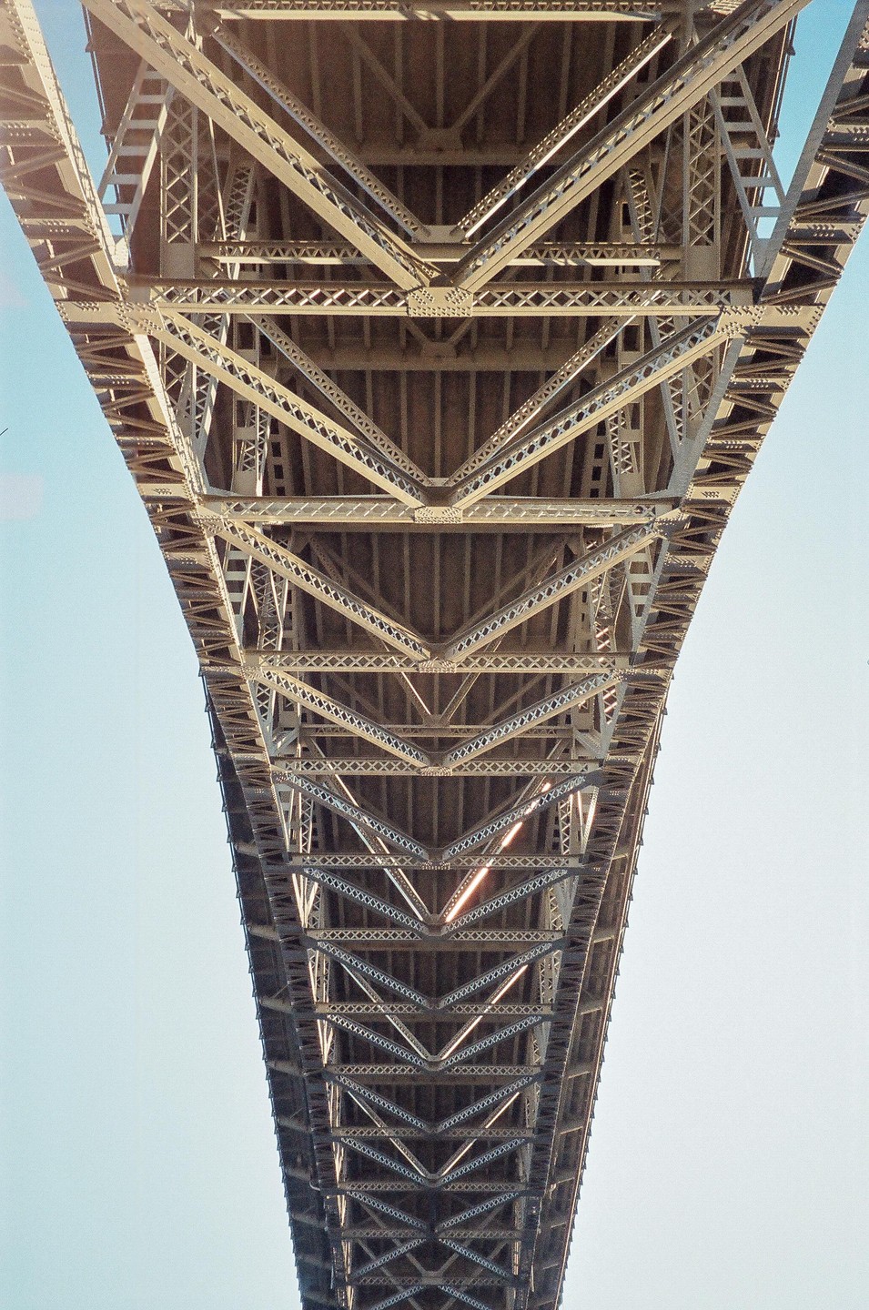 The underside of a large metal bridge is visible against a clear sky.