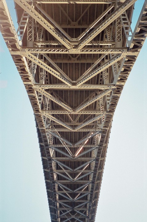The underside of a large metal bridge is visible against a clear sky.