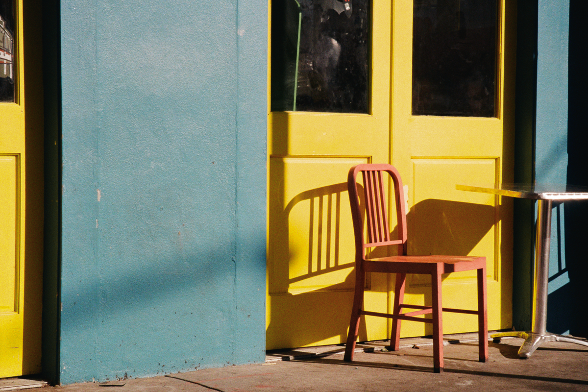 A red chair sits in front of a yellow door next to a blue wall with a small table.