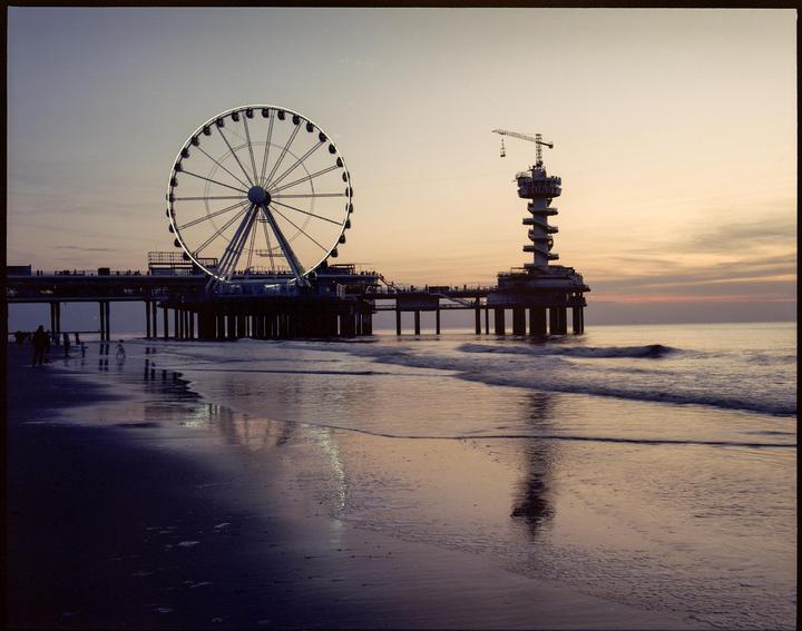A ferris wheel and a tower stand on a pier over the ocean at dusk.