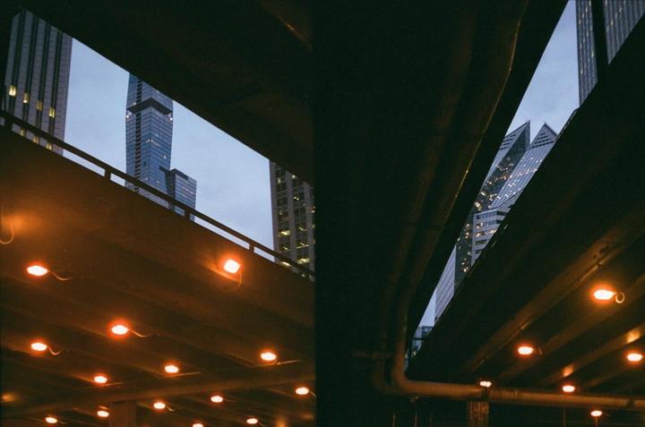 A view of skyscrapers through the gaps of an elevated road with orange lights.
