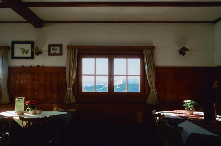 A window in a mountain hut looks out onto snowy mountains.