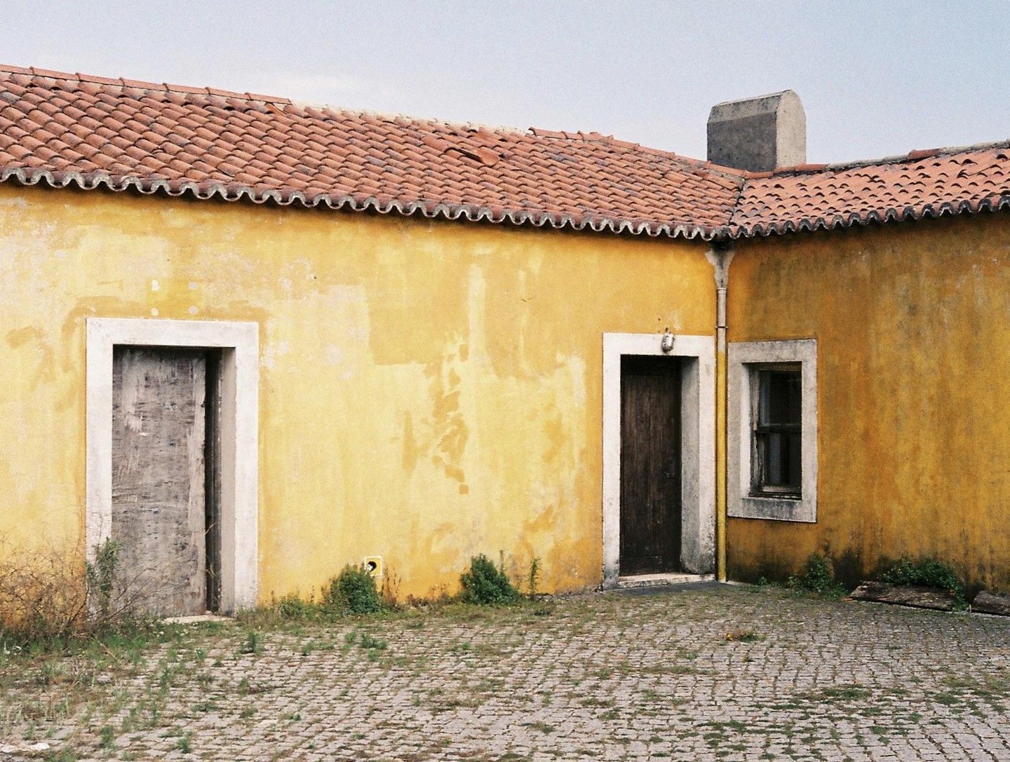 A yellow house with a red tile roof has two doors and one window.