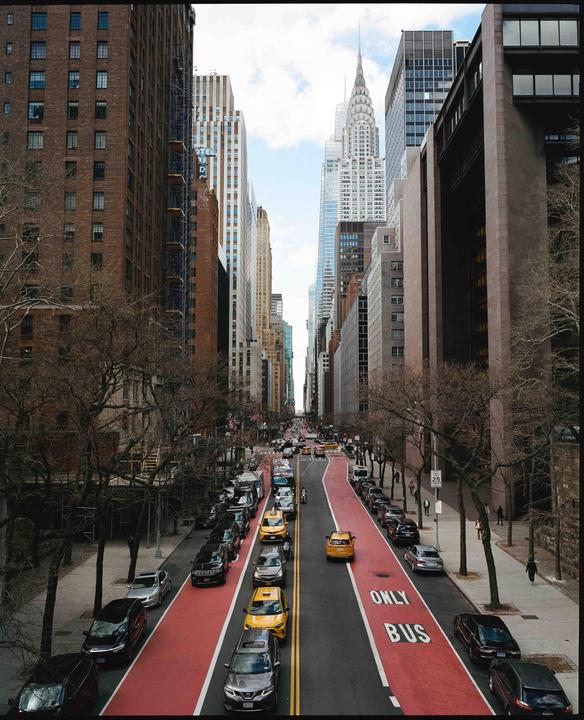 A street in New York City is filled with cars and taxis, with tall buildings and the Chrysler Building in the background.