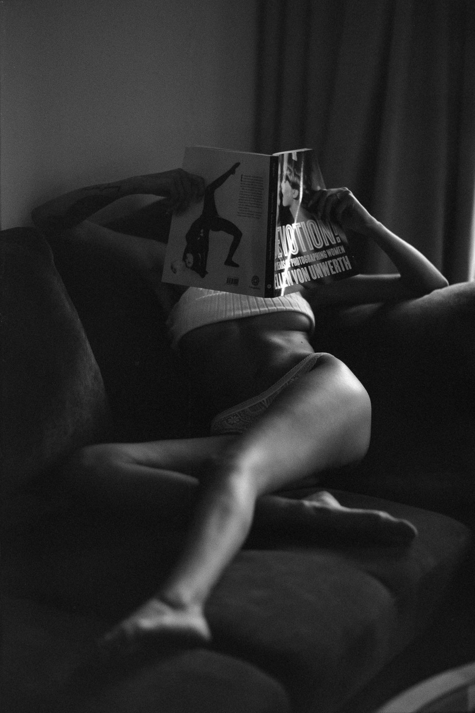 A woman in underwear is lying on a sofa and reading a book.