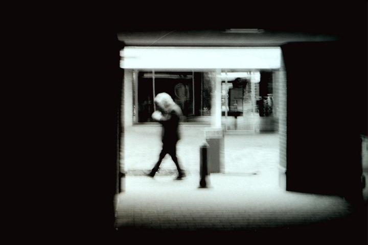 A blurry figure of a person walks through a brightly lit underpass.