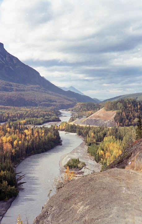 A winding river flows through a valley surrounded by mountains and autumn trees under a cloudy sky.