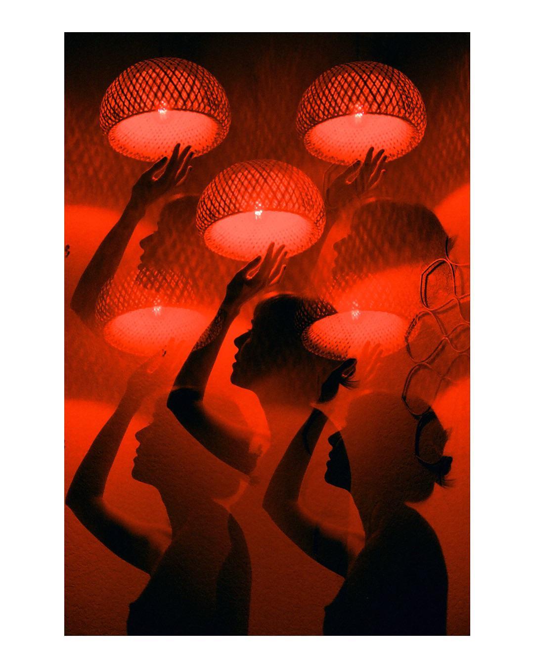 Multiple silhouettes of women are visible, some holding glowing woven lamps, against a red background.
