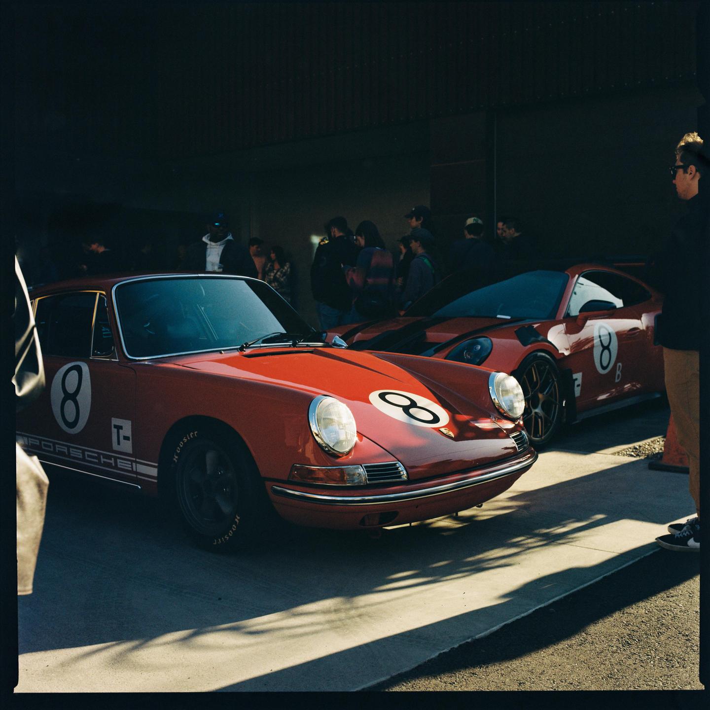 Two red Porsche cars with the number eight on them are parked in a garage with people standing around them.