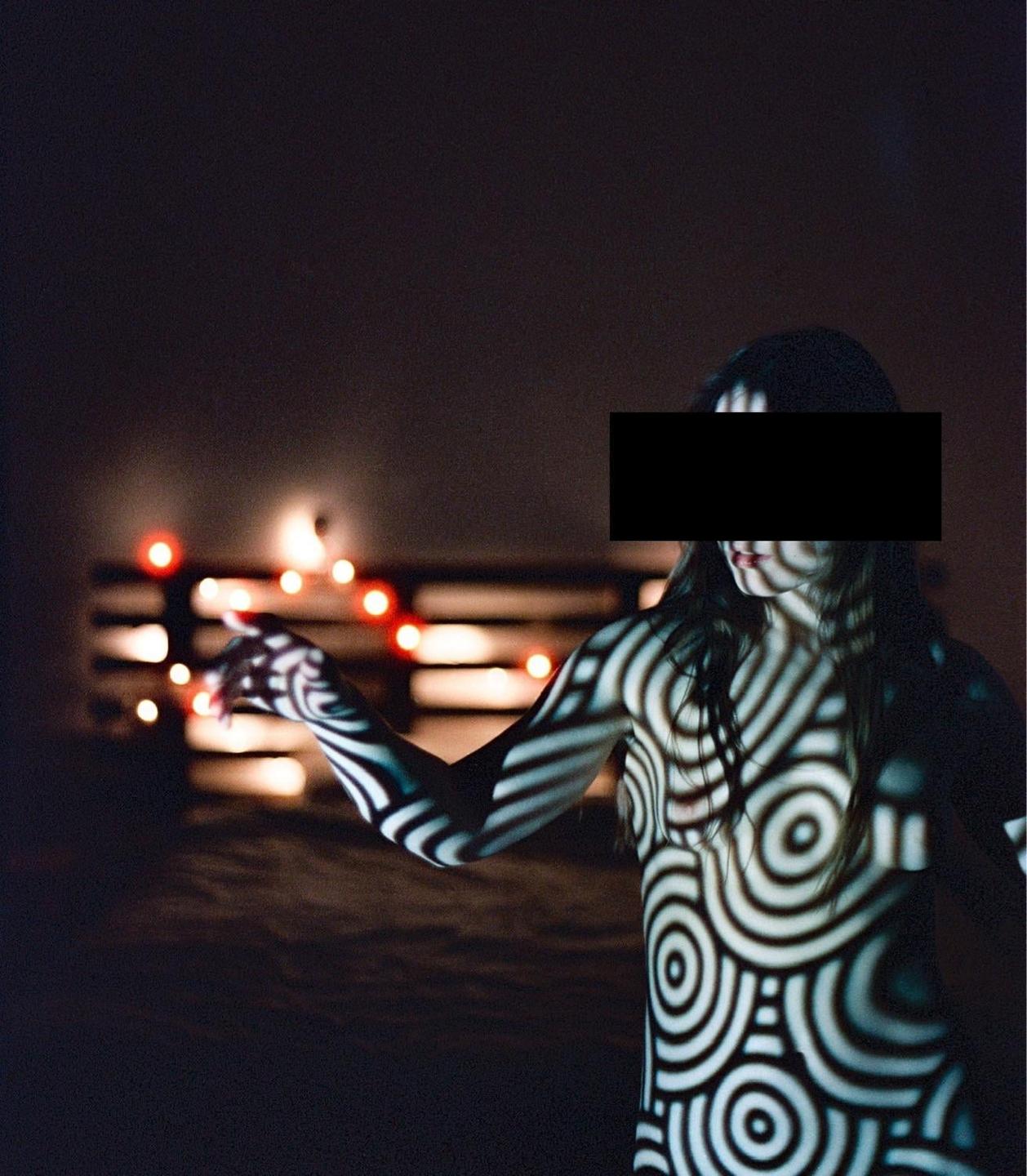 A woman is illuminated by a pattern of circles and lines, with string lights in the background.