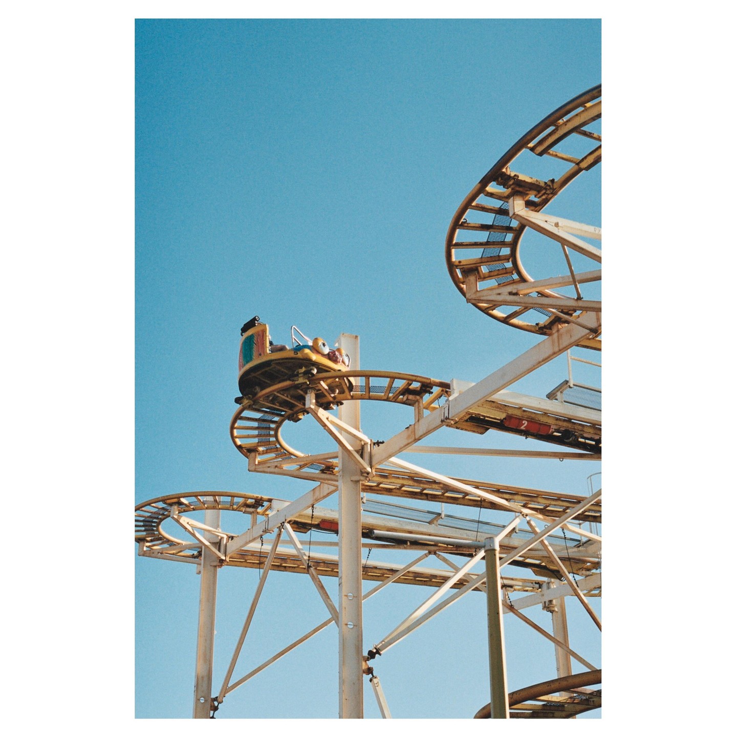 A yellow roller coaster car is on a track against a clear blue sky.