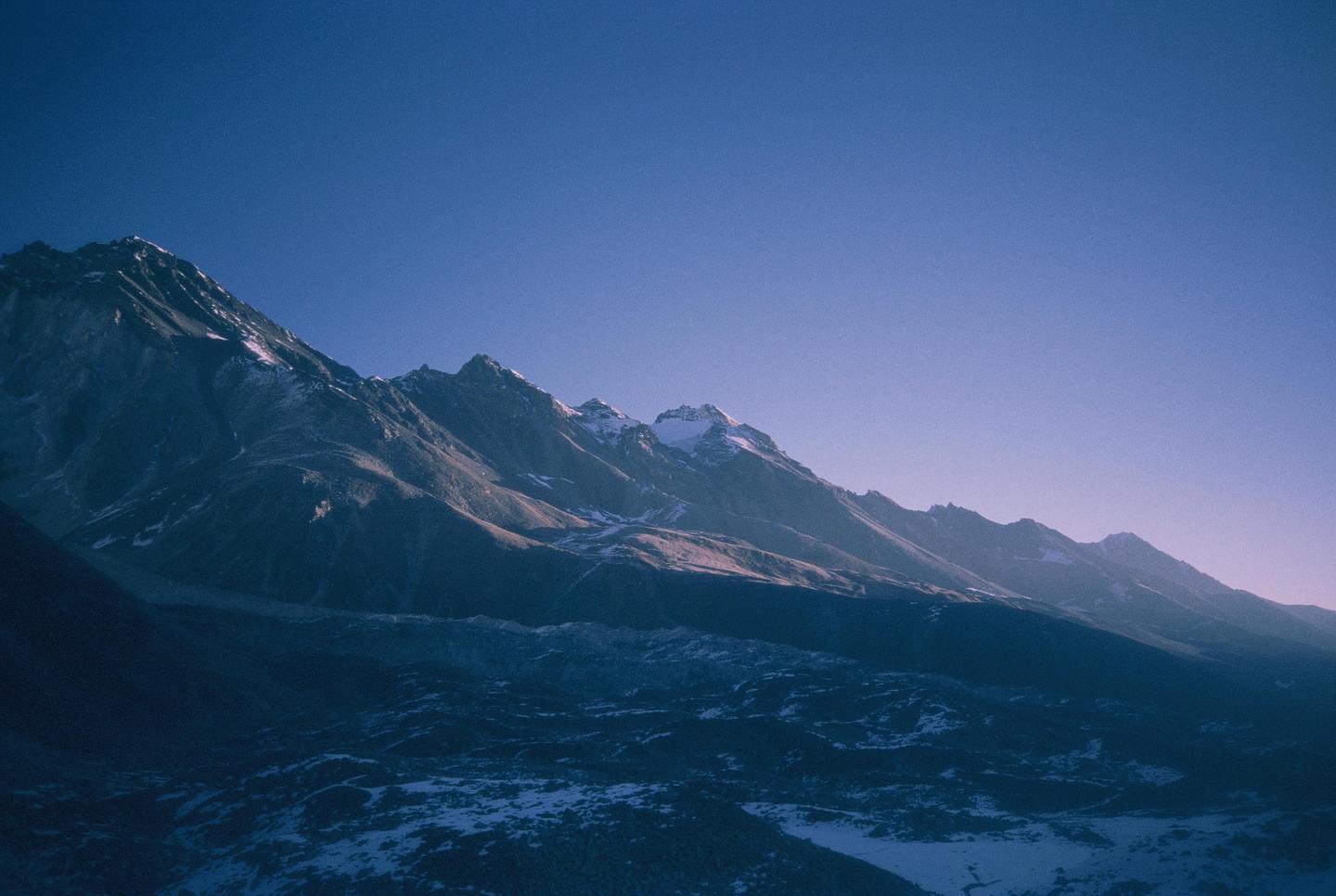Snow-capped mountains are illuminated by the sun under a clear sky.