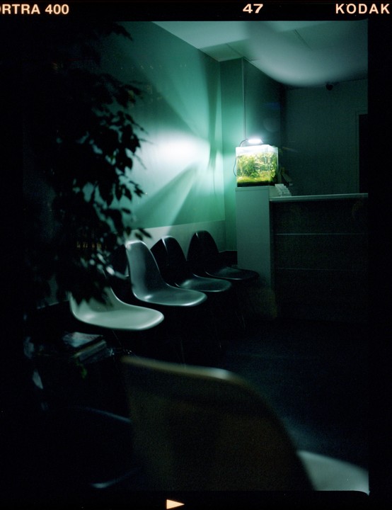 A dark waiting room features a row of chairs and a brightly lit aquarium on a counter.