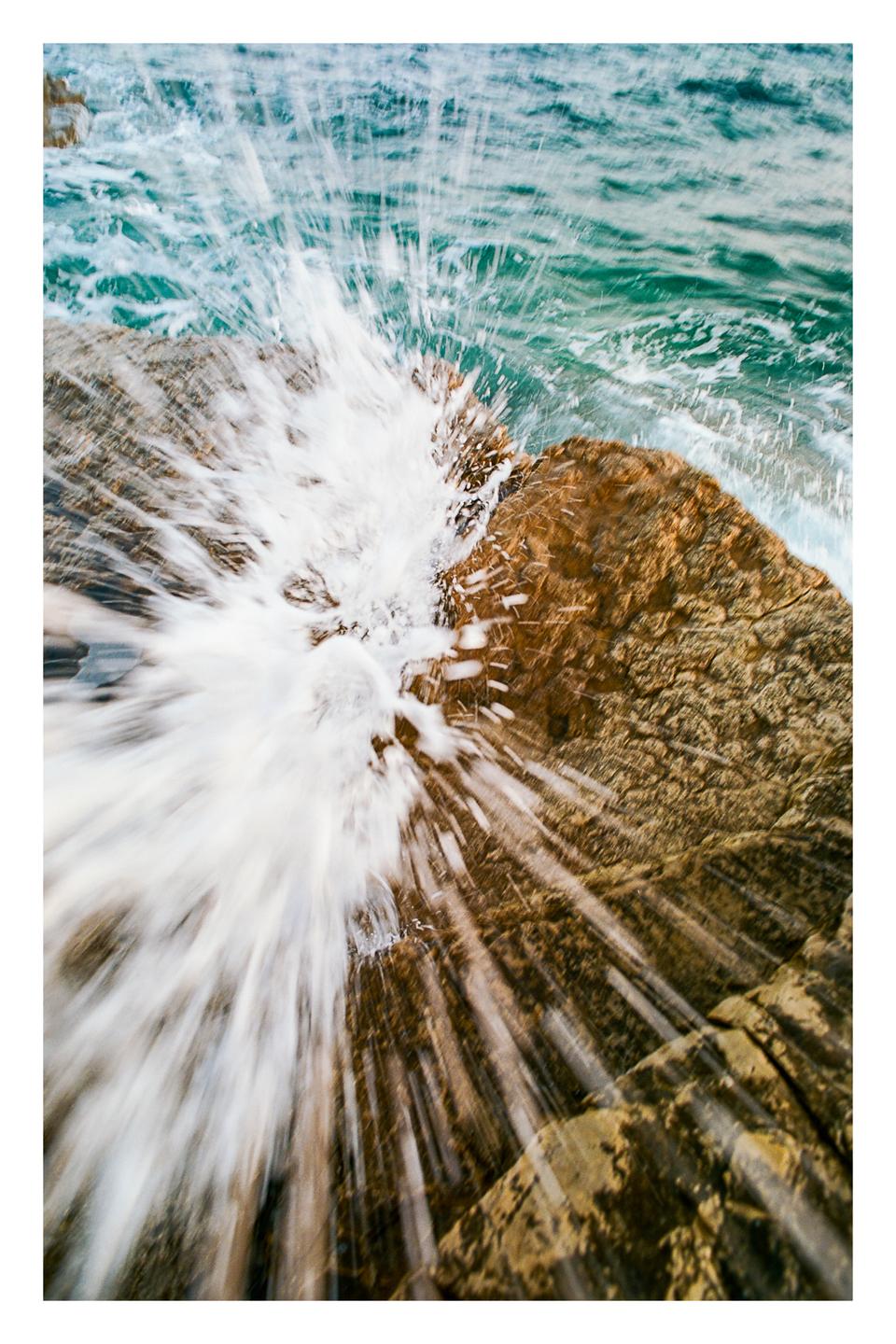 A wave crashes against a rock, sending water splashing into the air.