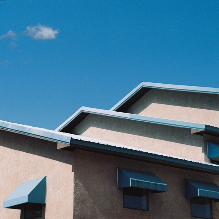 A building with blue awnings and roof trim is visible under a clear blue sky with a single cloud.