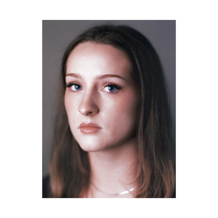 A woman with long hair and blue eyes looks directly at the viewer.