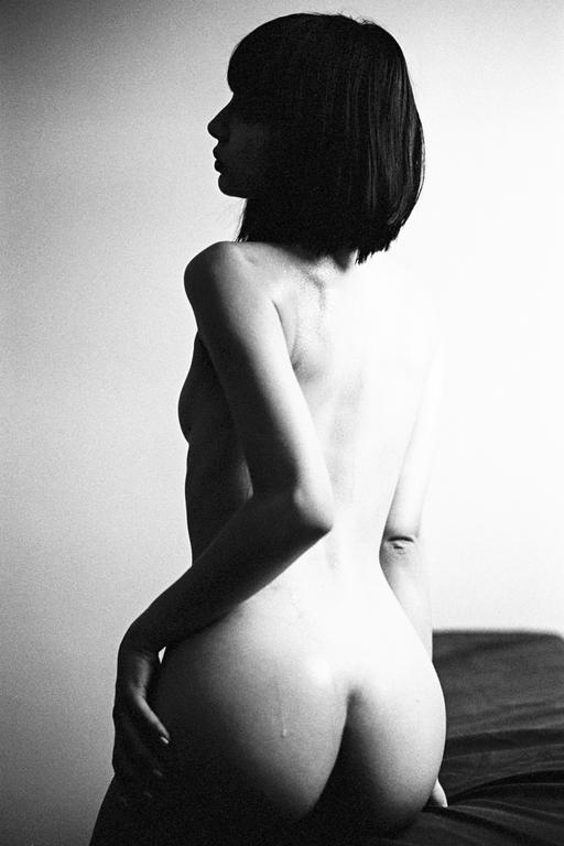 A woman with short hair is shown from behind, looking to the left, with a single drop of liquid visible on her left buttock.