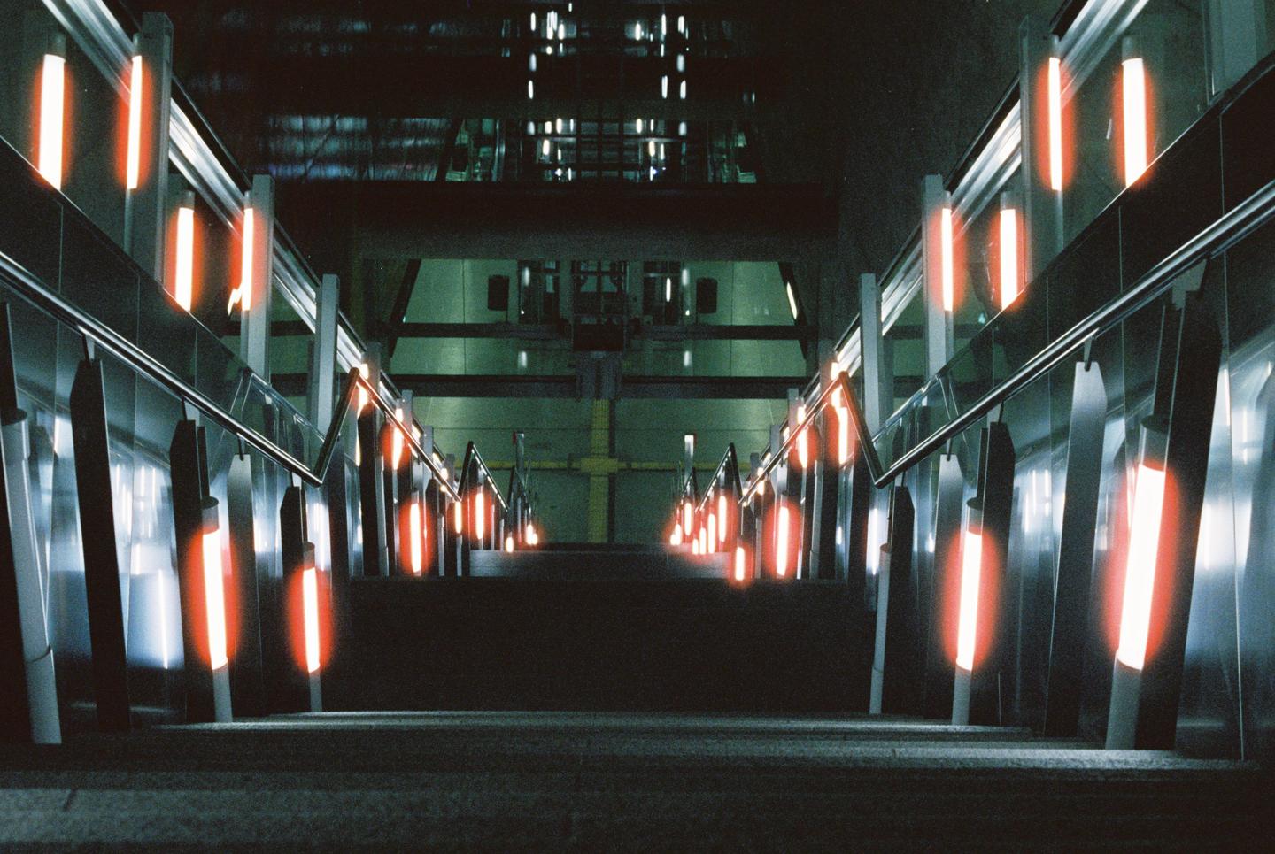 An escalator with orange lights descends into a dark subway station.
