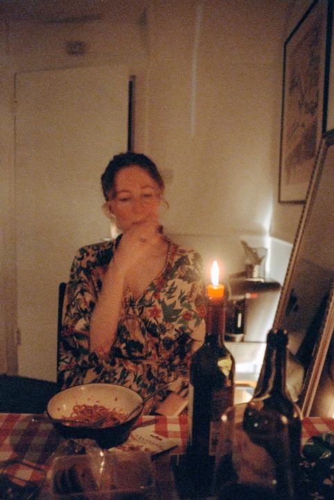 A woman sits at a table with a lit candle and a bowl of food.