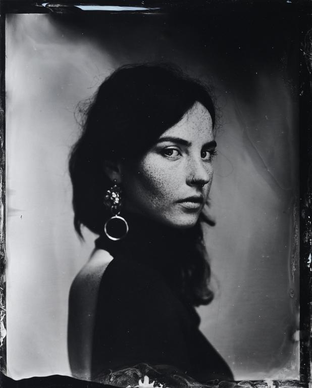 A woman with dark hair and freckles looks over her shoulder at the viewer.