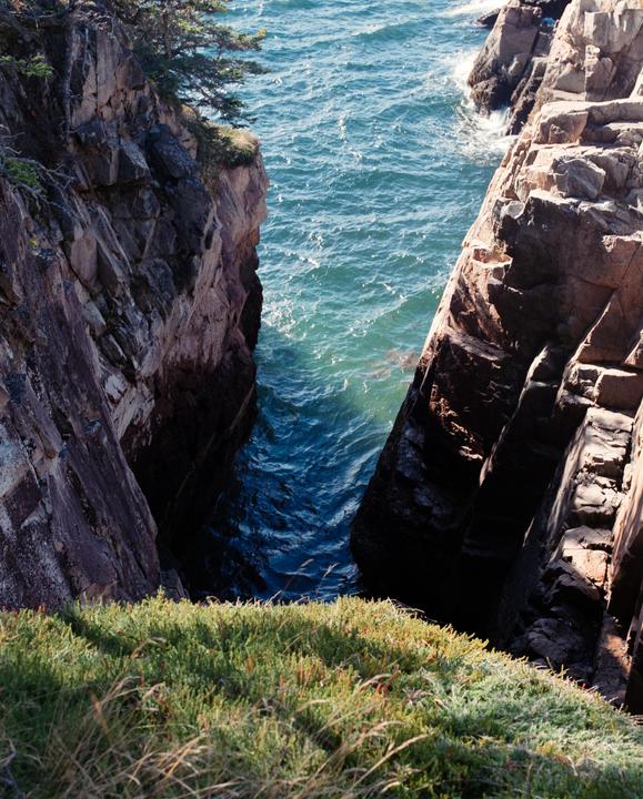 A narrow inlet of blue ocean water is visible between two rocky cliffs covered with green vegetation.
