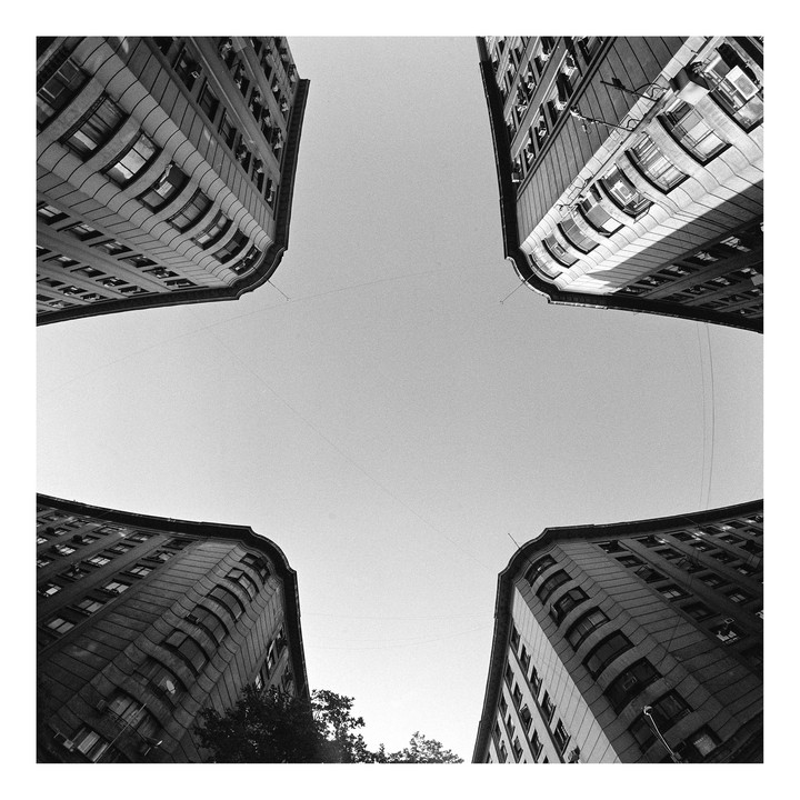 Four tall buildings with curved facades are seen from below, framing a clear sky.