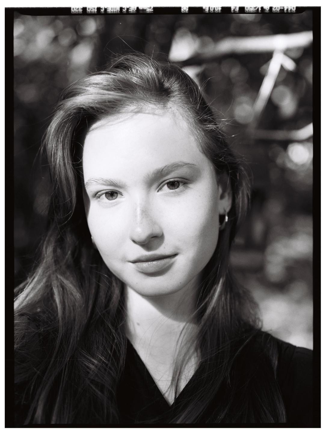 A young woman with long hair looks directly at the viewer in a black and white portrait.