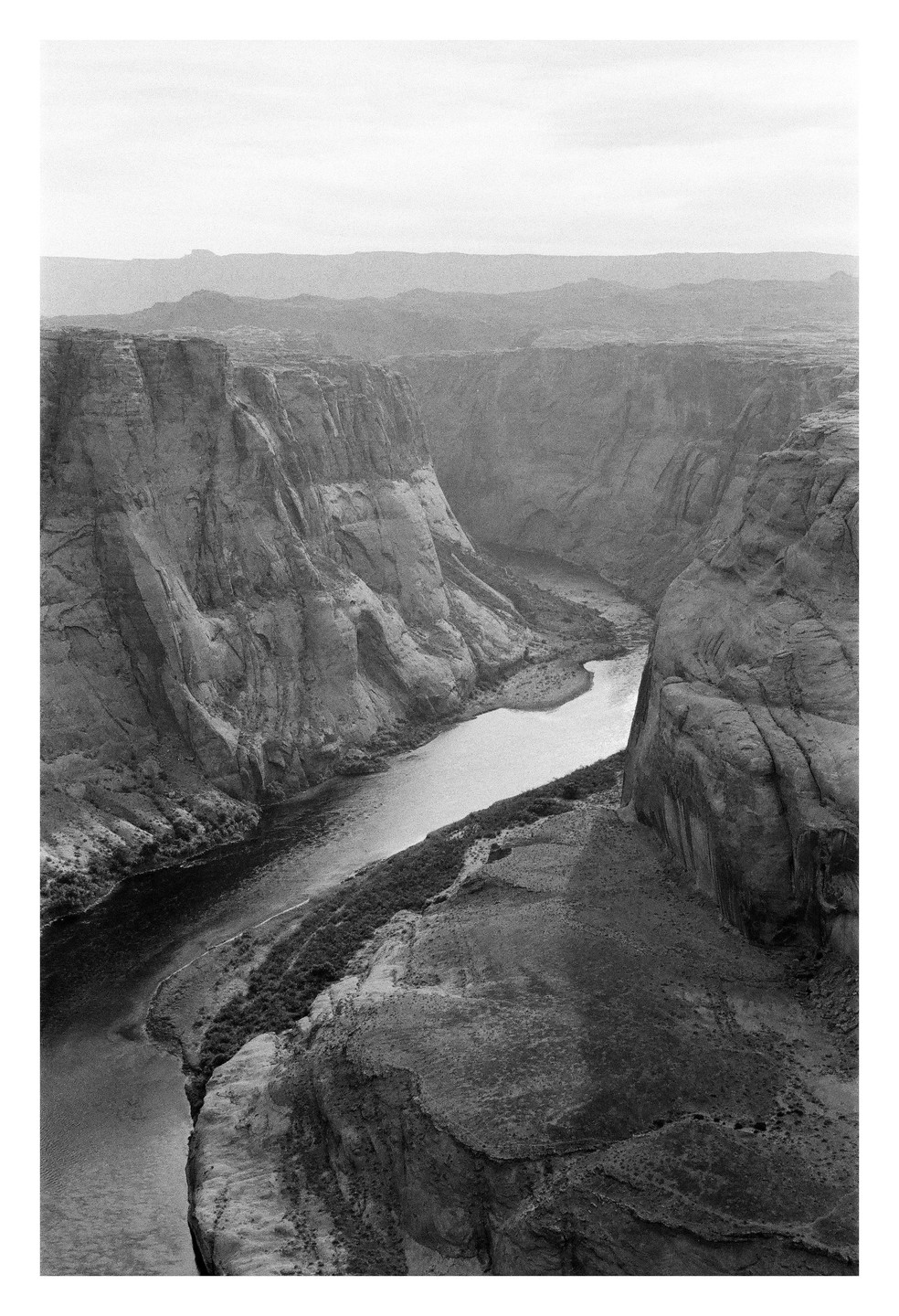 A river winds through a deep canyon with steep rock walls under a hazy sky.