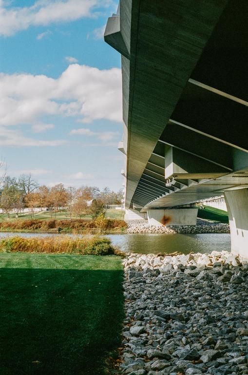 A concrete bridge spans over a river with green grass and rocks on the bank.