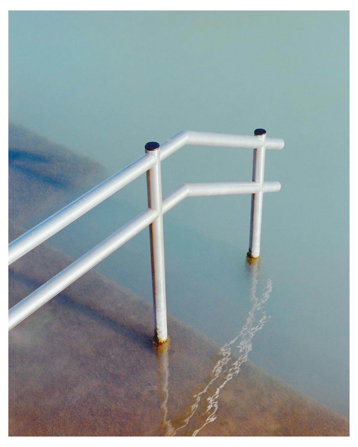 A metal handrail extends into a sea pool with light blue water.