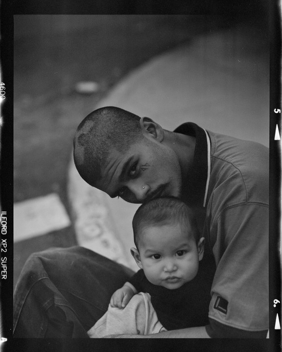 A man with a shaved head and a baby are looking towards the viewer.