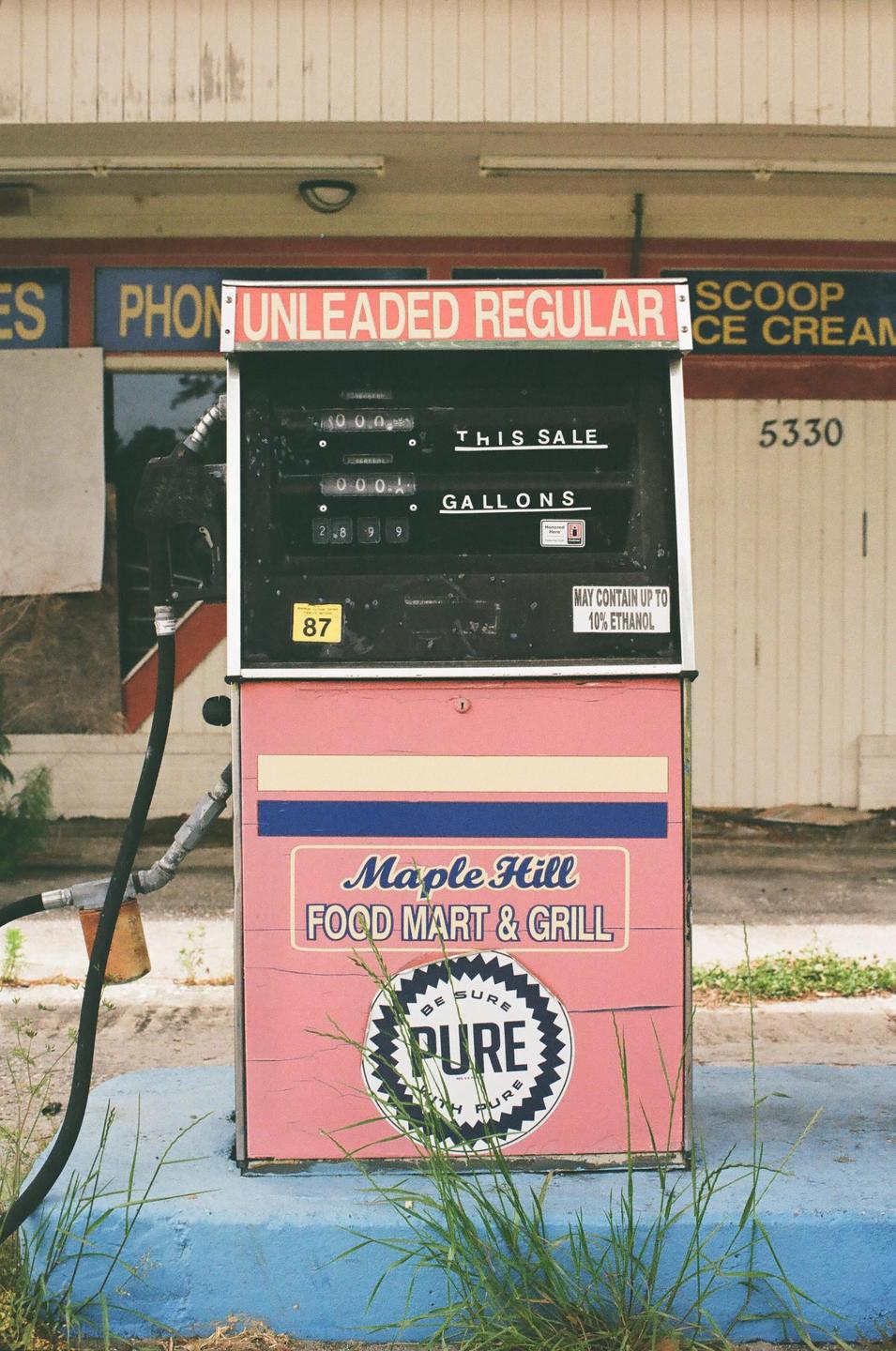 A pink gas pump with a black display stands in front of a building with a white and blue sign.