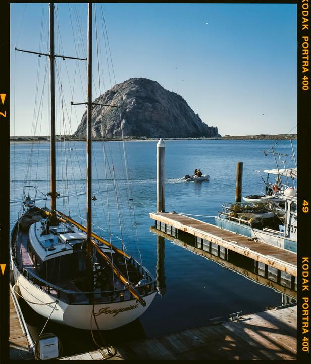 A sailboat is docked in a bay with a large rock formation in the background.