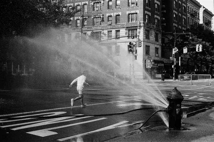 A child runs through water spraying from a fire hydrant on a city street.