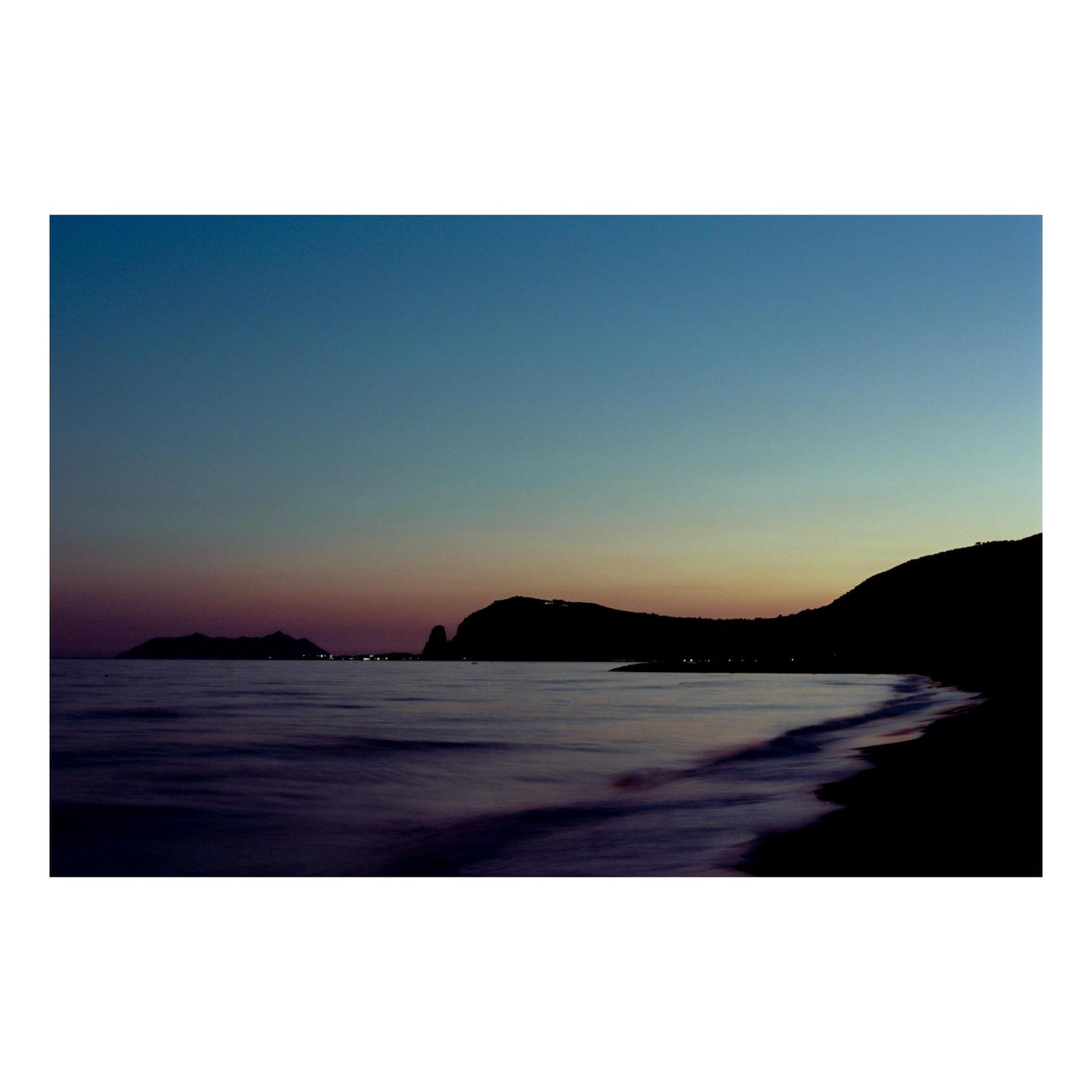 A long exposure photograph captures the coastline and sea at dusk with a gradient sky.